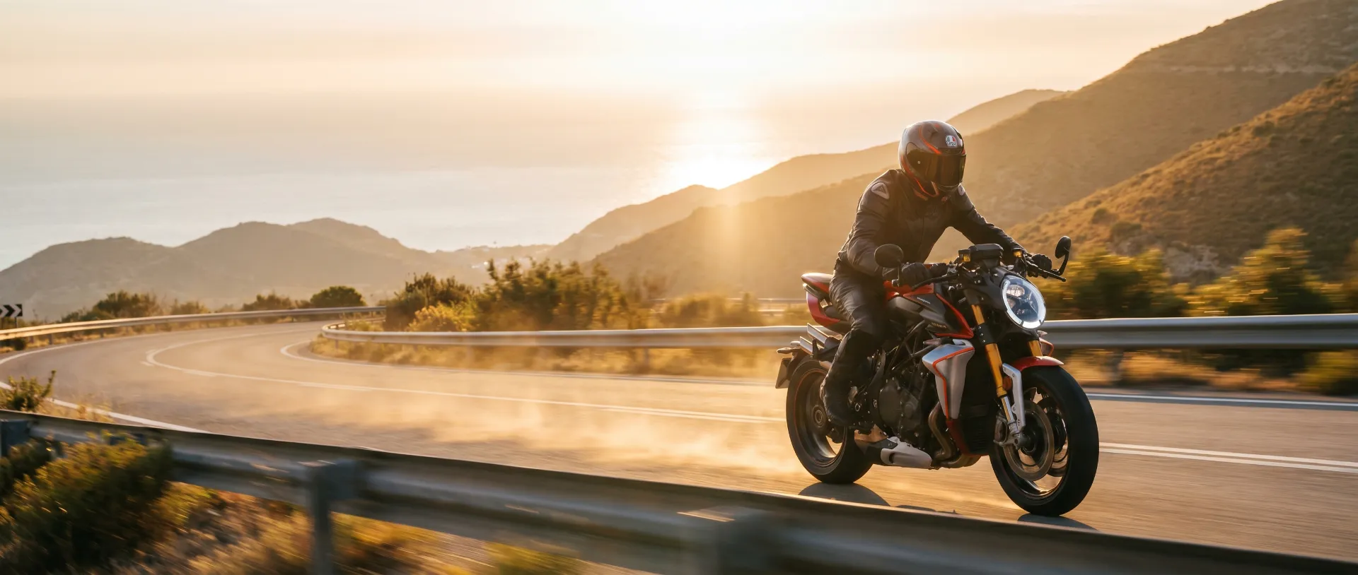 Motociclista in sella a una naked rossa su strada costiera al tramonto